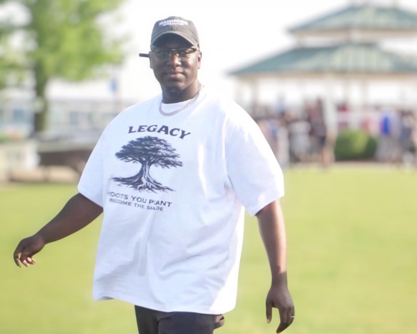Man wearing a white t-shirt with 'Legacy' text and graphic, standing on grass.